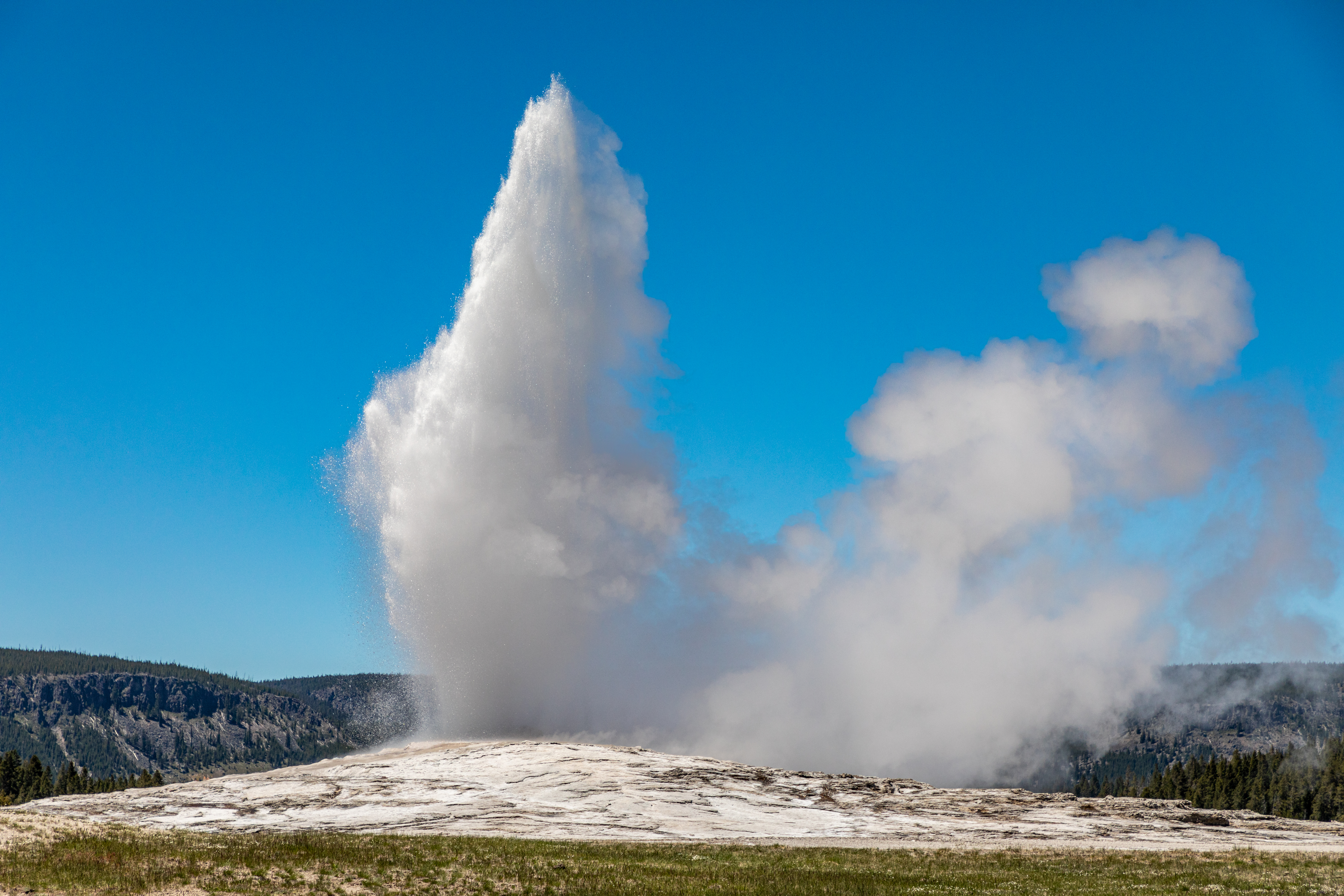 Old Faithful geyser erupting at Yellowstone National Park with mountains in background