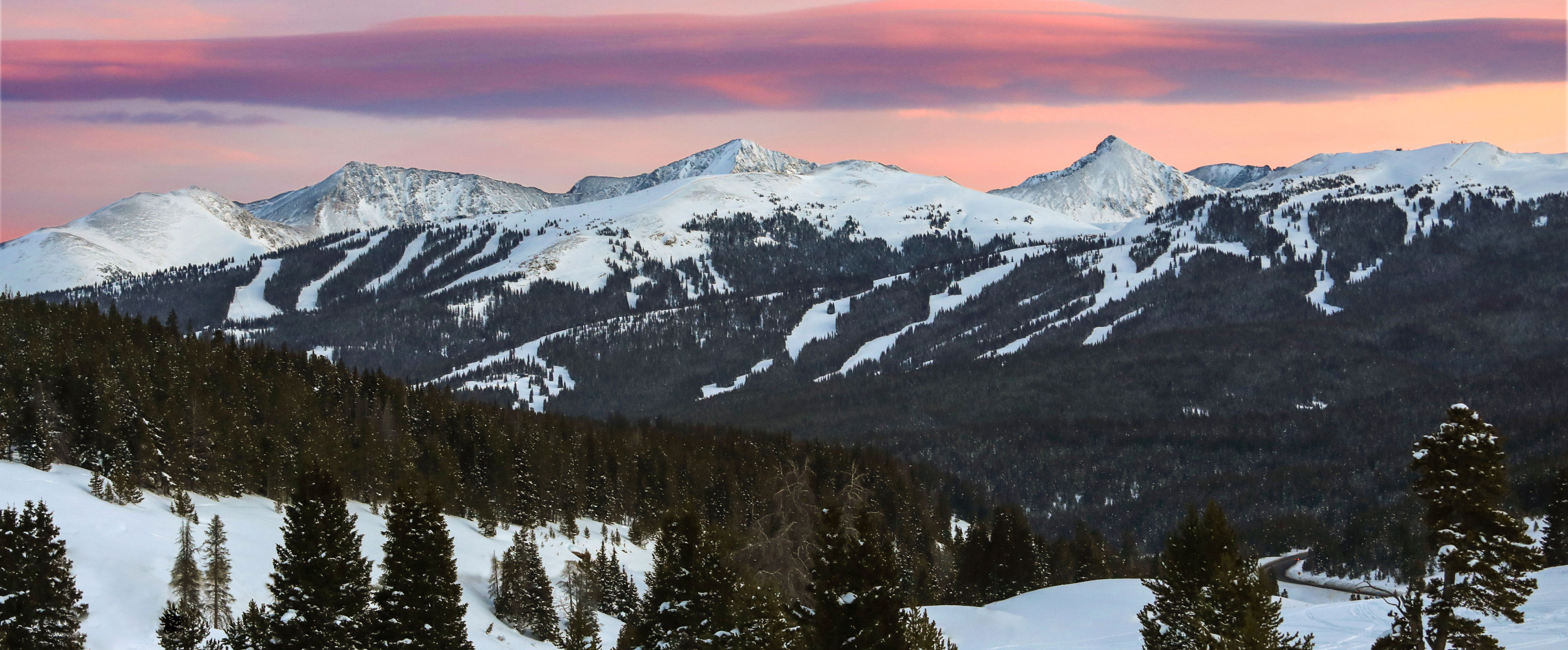 Panoramic view of snow-covered mountains at a Colorado ski resort with skiers descending slopes