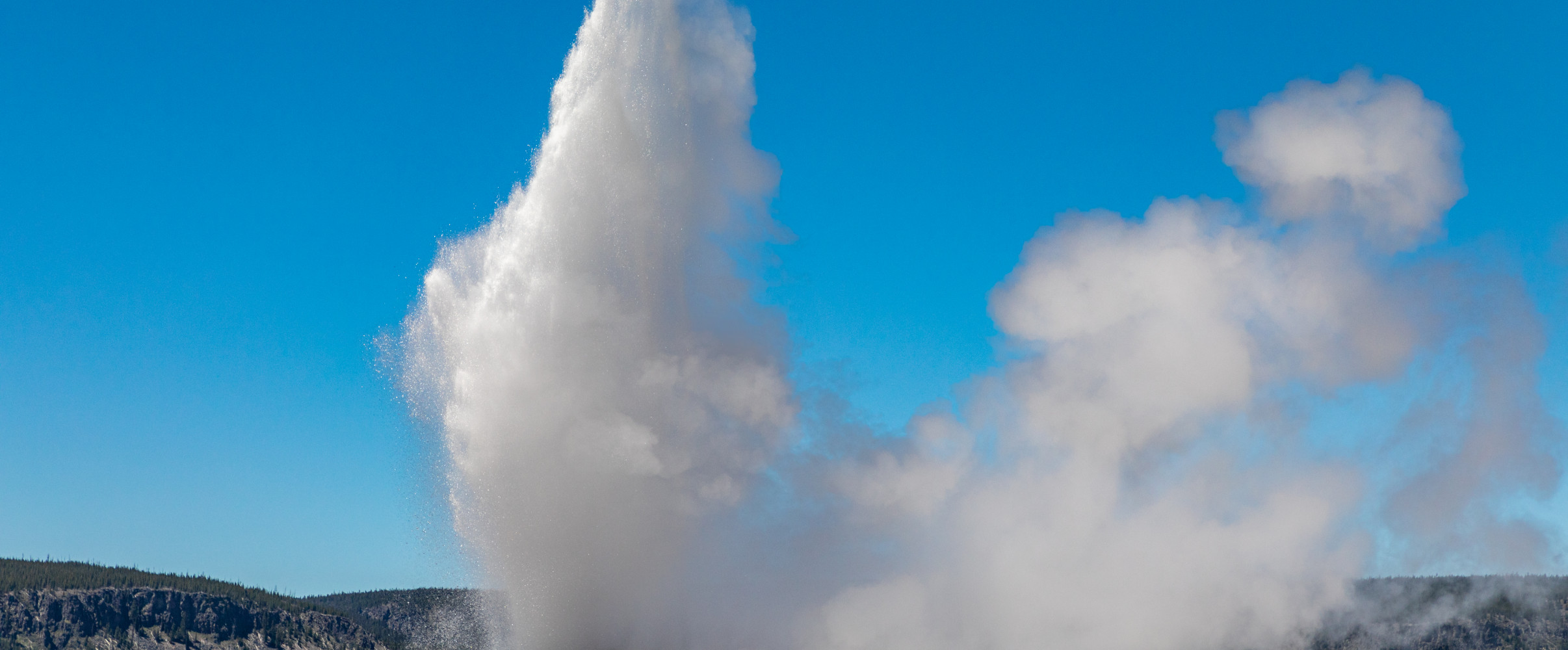 Old Faithful geyser erupting at Yellowstone National Park with mountains in background