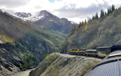 Passenger train winding through mountain landscape with snow-capped peaks