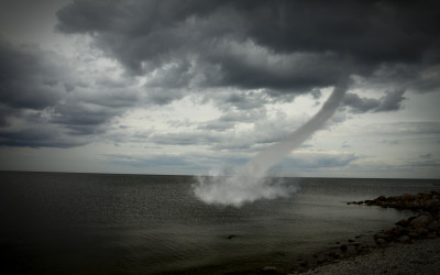 Powerful tornado touching down in rural landscape with dark stormy clouds