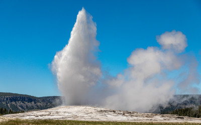 Old Faithful geyser erupting at Yellowstone National Park with mountains in background
