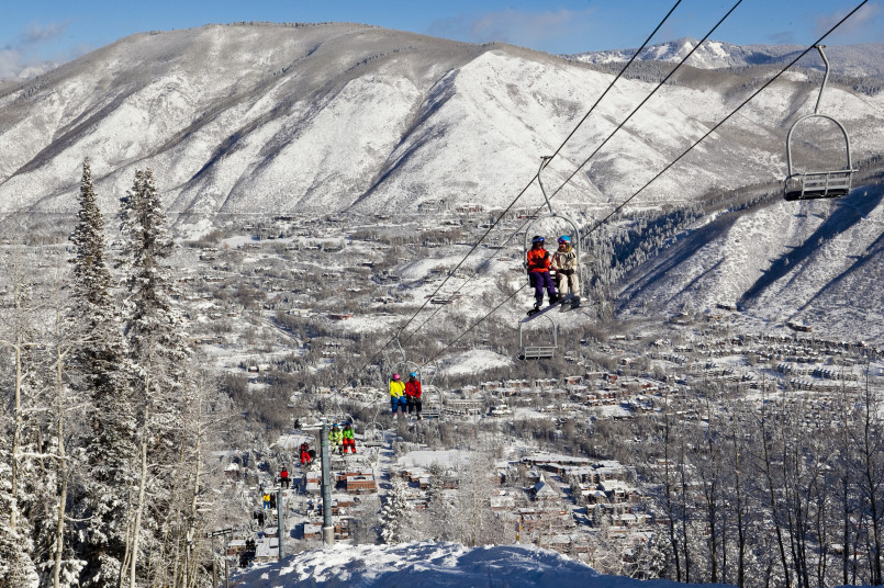 Skiers descending a groomed run at Aspen Snowmass with mountain backdrop