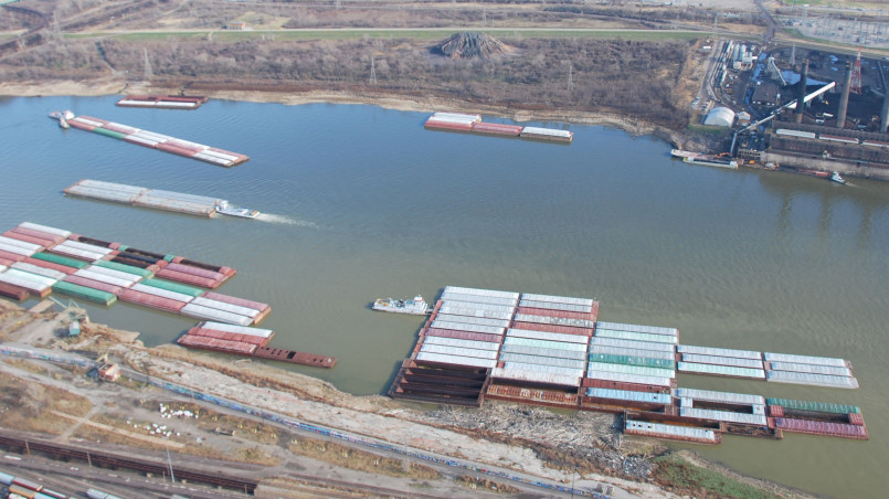 Barge traffic on Mississippi River Large barge convoy transporting cargo on the Mississippi River with industrial facilities visible along the shoreline