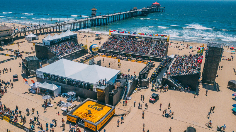 Professional beach volleyball players diving for a ball during a tournament with spectators on the beach
