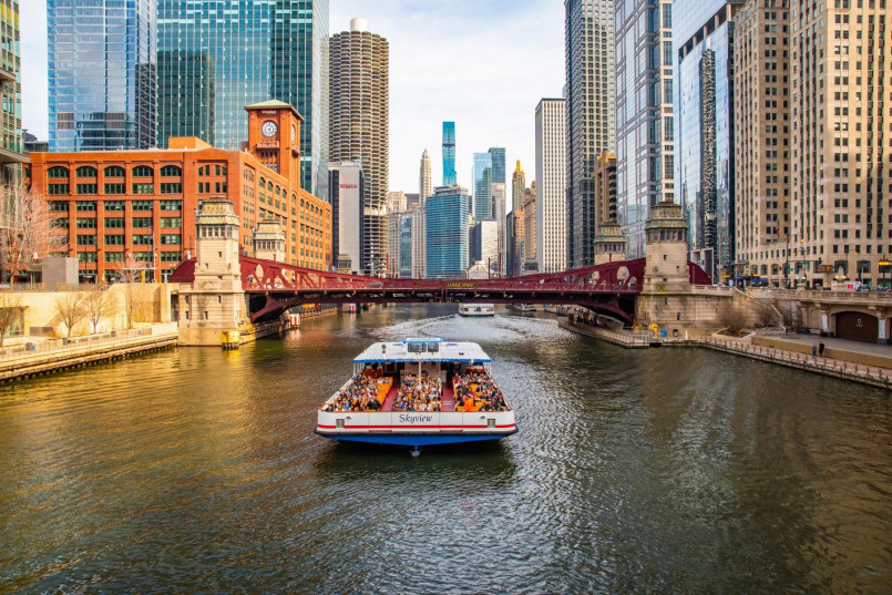 Chicago River with skyscrapers lining both sides and tour boats