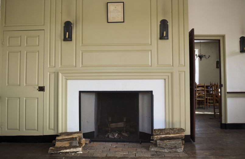 Colonial-era tavern room with large stone fireplace and wooden beams