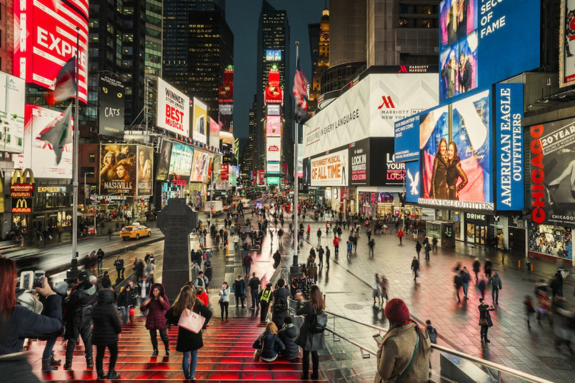 Crowds of pedestrians crossing at Times Square with bright billboards and city lights