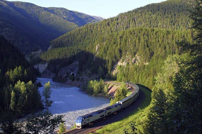 Empire Builder train passing through Glacier National Park with dramatic mountain scenery and pine forests in the background