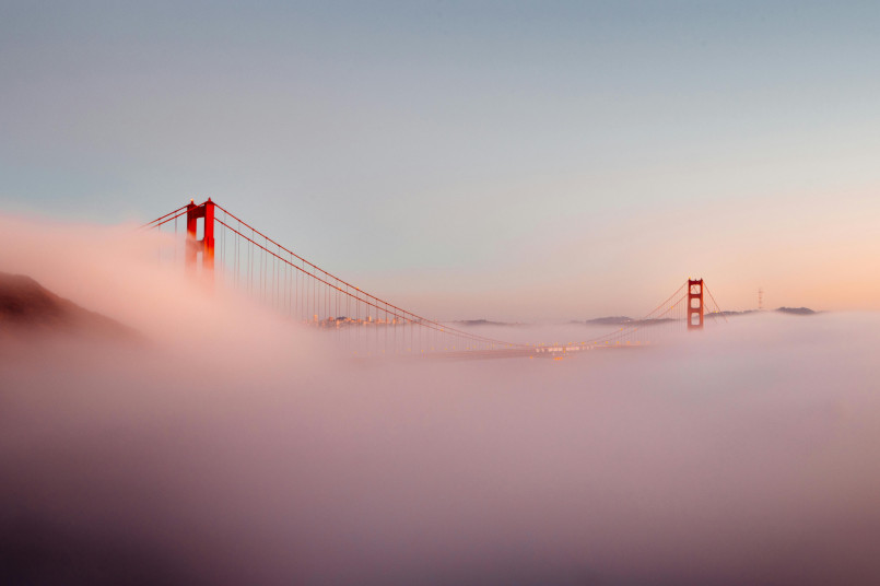 Golden Gate Bridge partially shrouded in fog with San Francisco skyline in background