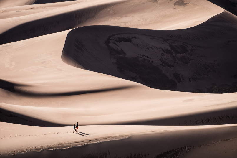 Star-filled night sky over sand dunes with mountains in background