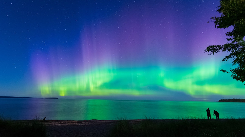 Northern lights michigan upper peninsula lake superior Green aurora borealis reflected in Lake Superior waters with silhouetted trees in foreground