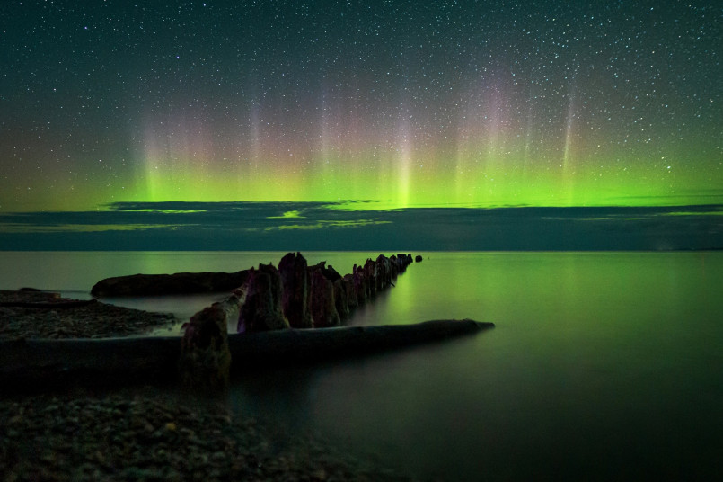Northern lights michigan upper peninsula lake superior Green aurora borealis reflected in Lake Superior waters with silhouetted trees in foreground