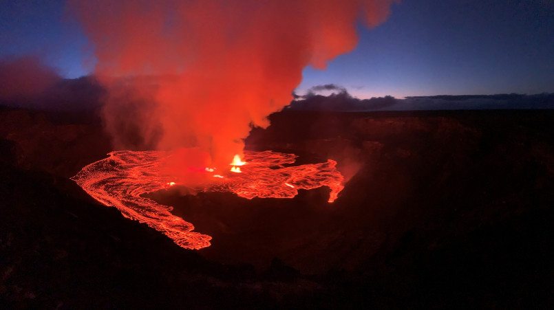 Glowing red lava flowing from Kilauea volcano at night against a dark landscape in Hawaii Volcanoes National Park