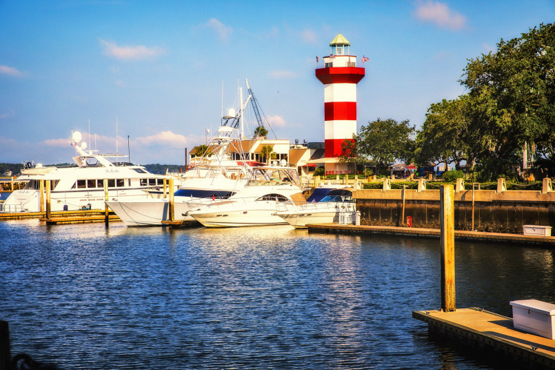 Red and white striped Harbour Town lighthouse with sailboats docked in marina and blue sky