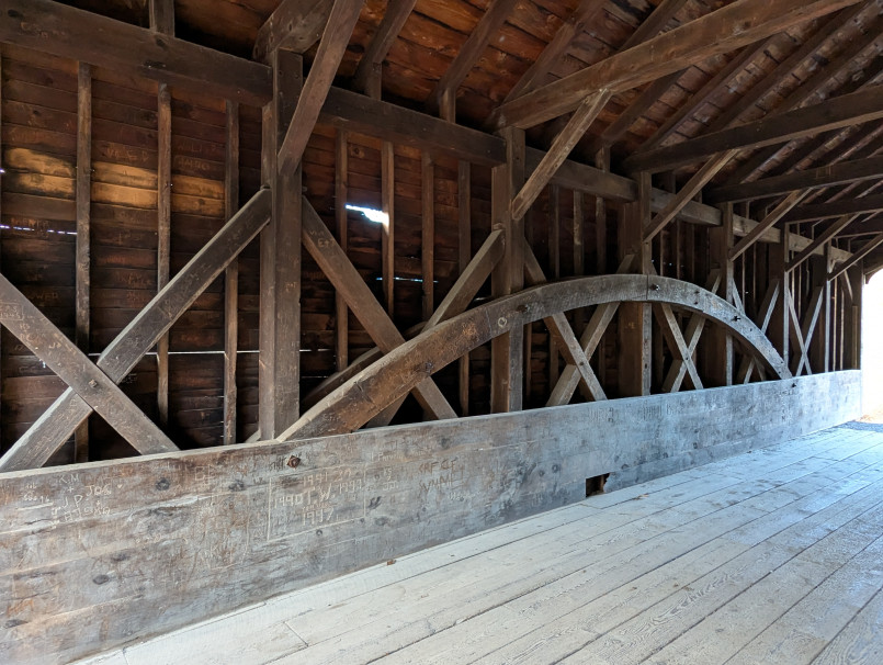 Interior view of a covered bridge showing wooden beam construction and light at the end