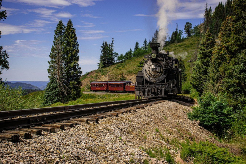 Historic steam locomotive of the Cumbres & Toltec Railroad crossing Cumbres Pass with plumes of smoke against a backdrop of mountain scenery