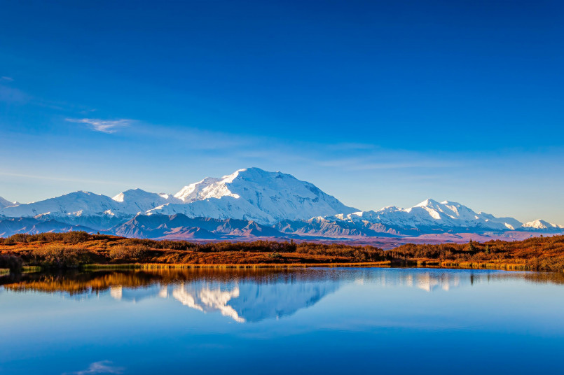 Majestic snow-covered Denali mountain reflected in a calm lake with tundra in foreground