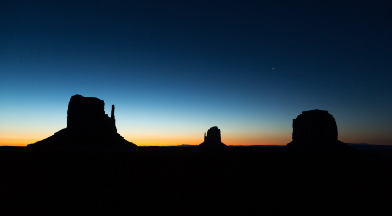 Red sandstone buttes of Monument Valley silhouetted against a golden sunrise sky