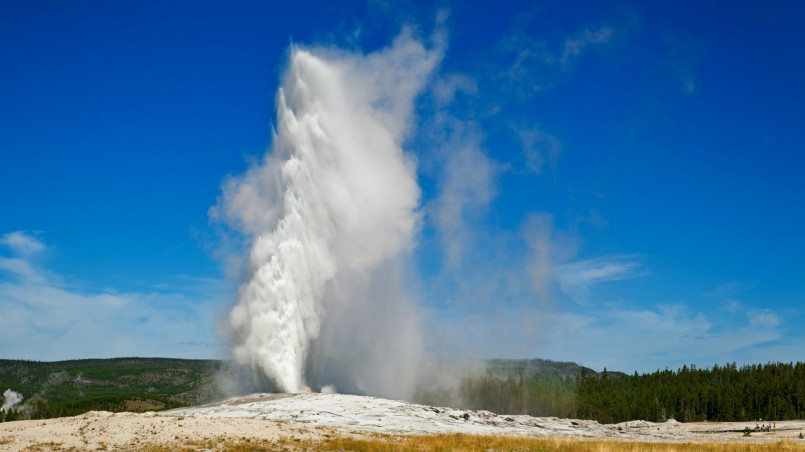 Old Faithful geyser erupting with a large plume of steam and water against blue sky