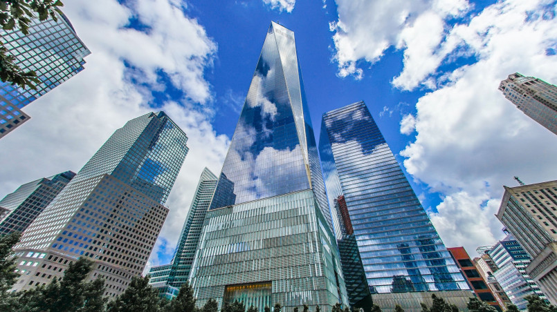 One World Trade Center with its glass facade reflecting blue sky and clouds