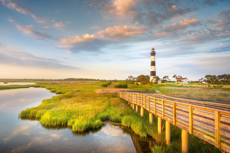 Black and white spiral Cape Hatteras lighthouse against blue sky with beach grasses in foreground