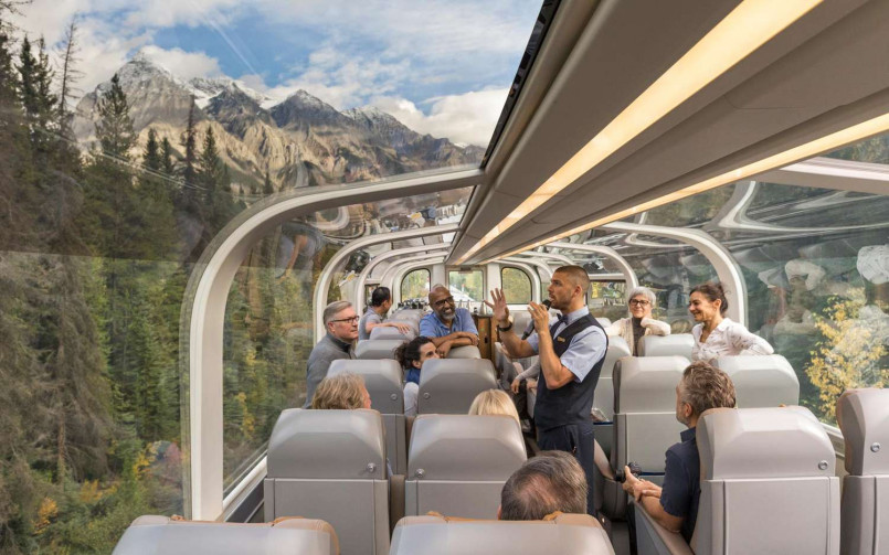 Passengers enjoying views from the glass-domed coach of the Rocky Mountaineer as it travels alongside the Colorado River with red rock formations visible