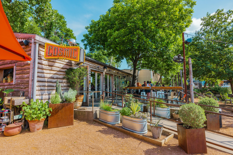 People enjoying coffee on a sunny patio at an Austin coffee shop with string lights and local artwork