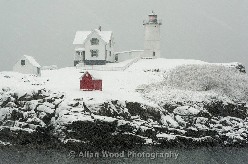Maine lighthouse winter storm, coastal snow Snow-covered lighthouse on rocky Maine coast during a winter storm with crashing waves