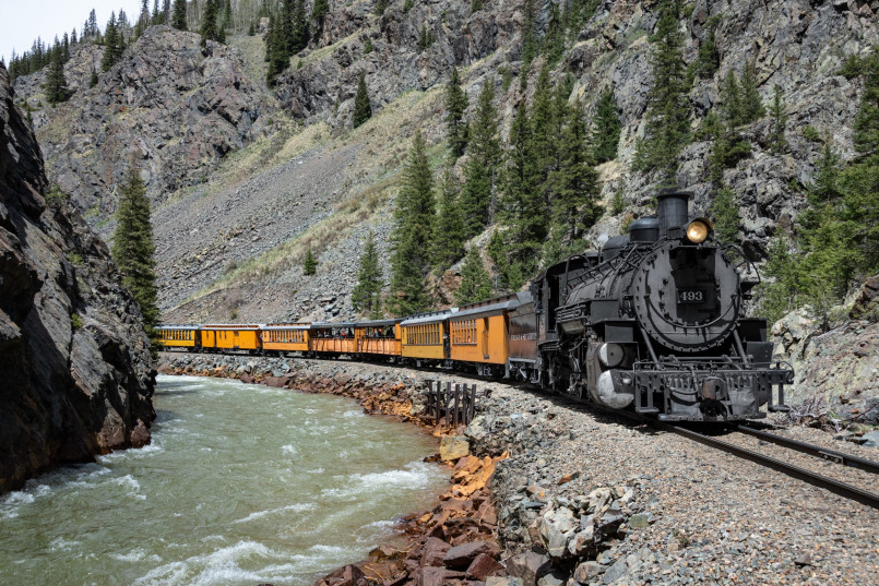 Steam-powered locomotive of the Durango & Silverton Railroad traversing a cliff edge with the Animas River far below
