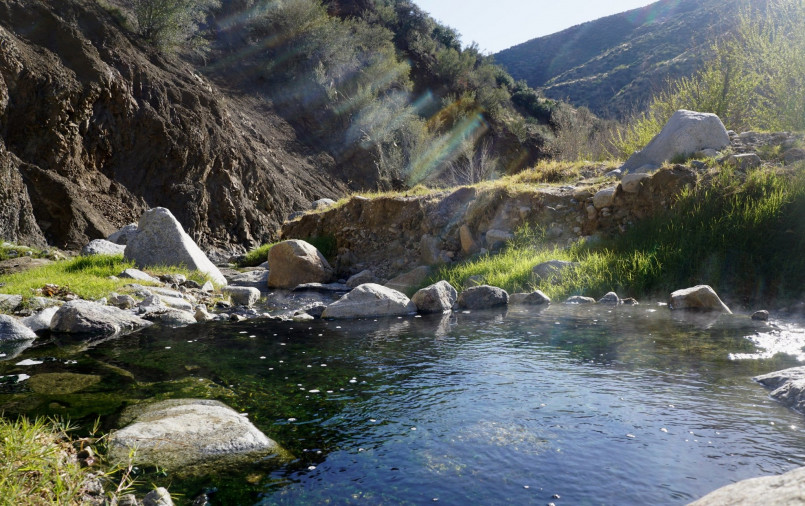 Steaming natural hot spring surrounded by forest with a small tent campsite nearby