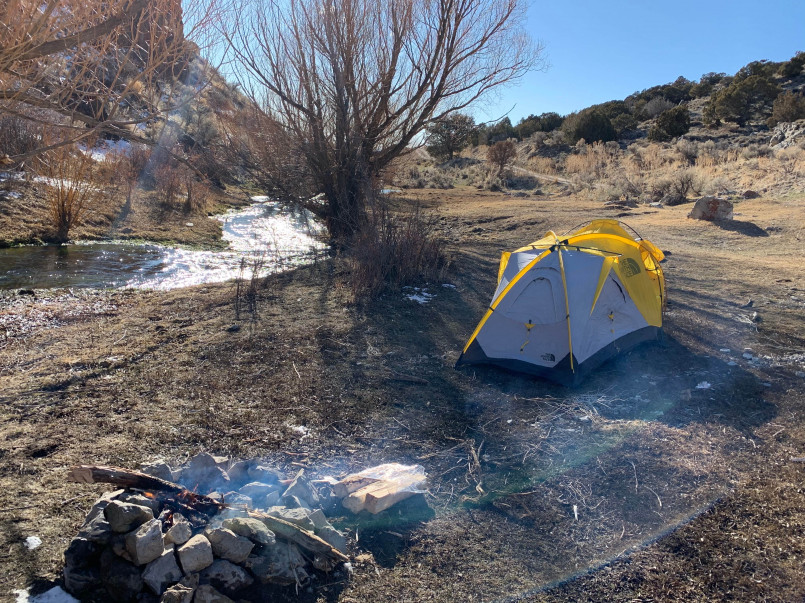 Wilderness hot springs camping Steaming natural hot spring surrounded by forest with a small tent campsite nearby