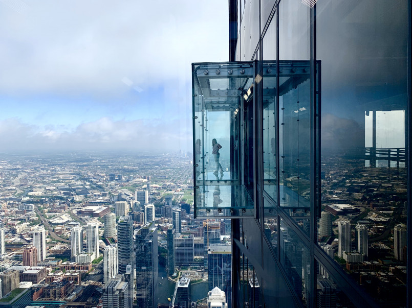 Tourists standing on the glass balcony Skydeck of Willis Tower with Chicago cityscape below